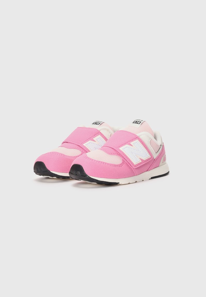Un par de zapatillas infantiles rosas y blancas con tiras de velcro y suelas negras sobre un fondo blanco.