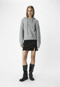 Grå ribbade sweatshirt med dragsko, svart corduroykjol med en sidoklyvning och knälång svarta läderstövlar med spännen.