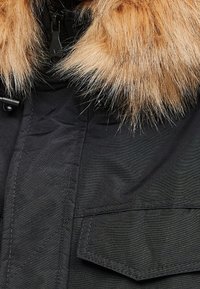 Černá parka s odnímatelným béžovým kožešinovým límcem, se zipovým zavíráním a náprsními kapsami vpředu.