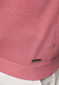 Maglione a maglia rosa chiaro con orlo a coste, dotato di una piccola etichetta metallica logo sul bordo inferiore. Tessuto morbido, design a vestibilità standard.
