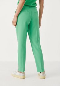 Persoon staat in een helder groen op maat gemaakte broek, een bijpassend topje en witte sneakers met lichtbruine zolen.