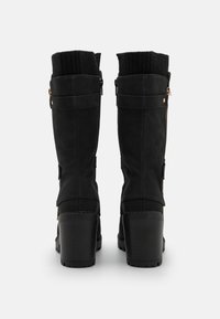 Bottes hautes noires en daim jusqu'au genou avec bordure en tricot, fermetures éclair latérales, garnitures ton or et talons noirs texturés. Fini lisse avec design structuré.