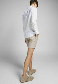 Valkoinen nappikauluspaita, jossa on pieniä sinisiä pisteitä, beigeet shortsit ja vaaleanruskeat nubukkinahkakengät. Paidassa on klassinen kaulus ja pitkät hihat.