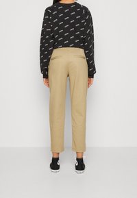 Pantalons chino kaki fuselés avec deux poches arrière, associés à un sweatshirt graphique noir affichant un texte blanc répété. Stylé avec des baskets noires.