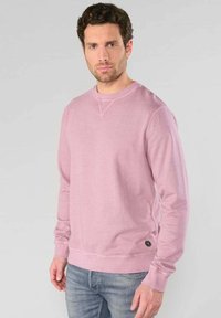 Felpa rosa chiaro realizzata in morbido tessuto, con colletto rotondo, polsini a coste e un discreto logo sul fondo.