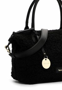 Sac à main noir texturé avec deux petites poignées, une longue bandoulière amovible et une étiquette ronde en métal doré attachée près de la poignée.