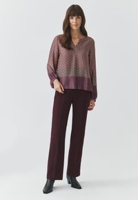 Rood en blauw bedrukt blouse met lange mouwen en een V-hals, gecombineerd met bordeaux brede pantalons en zwarte enkellaarsjes met hak.