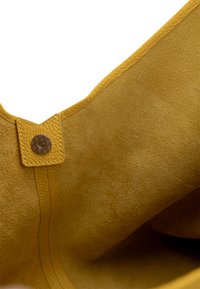 Sárga velúr táska sima külső felülettel, lekerekített V-alakú tetejével, bőrdíszítéssel és dekoratív patentgomb zárással.