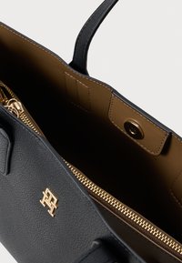 Must Blacki tekstuuriga nahast käekott, millel on kuldne tõmblukk ja riistvara, pruuni interjööri ning välise logodetailiga.