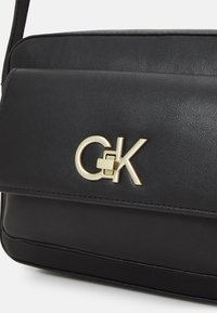 Černá kožená crossbody taška s překlápěcím víkem, se zlatým logem a texturovaným povrchem. Kompaktní design s popruhem na rameno.