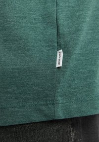 Zielona bawełniana koszulka z miękką teksturą, z metką na dolnym szwie, na której widnieje napis "JACK & JONES".