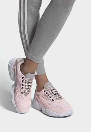 Zapatillas deportivas rosas con detalles de malla, suela blanca gruesa y diseño de cordones. Llevadas con pantalones ajustados grises con rayas laterales.