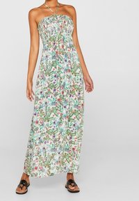 Maxikjole med et stropløst, draperet skær, der har et blomstermønster i grøn, rød og lilla på en lys baggrund.