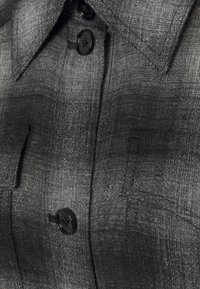 Černá a šedá kostkovaná košile na knoflíky s pevným límcem, viditelným šitím a černými knoflíky s texturovaným povrchem.