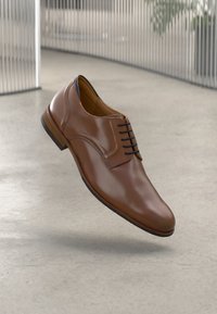 Braune Lederdressschuhe mit glatter Oberfläche, runder Zehenform, minimalistischer Gestaltung und schwarzen Schnürsenkeln. Hochgezogener brauner Absatz mit leichtem Glanz.