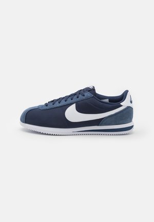 Marineblaue Sneakers aus einer Mischung von Stoff und Wildleder, mit einem weißen Nike-Swoosh, strukturierten Gummisohlen, abgerundeter Zehenpartie und kontrastierenden Fersendetails.