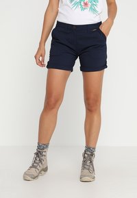 Mörkblå shorts i hållbart material med uppvikta fållar, framfickor och en liten logotagg på midjan. Kombinerade med grå vandringsskor.