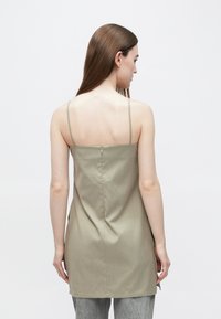Olivno zelena zgornja majica brez rokavov s tankimi naramnicami, s prilegajočim se pasom in zadrgo zadaj, izdelana iz gladkega, teksturiranega blaga.