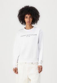 Bijela dukserica od mješavine pamuka s rebrastim rukavima i donjim rubom. Sadrži crni logo "TOMMY HILFIGER EST. 1985" sprijeda.
