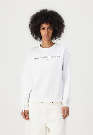Sudadera blanca hecha de una mezcla de algodón con puños y dobladillo acanalados. Presenta el logotipo "TOMMY HILFIGER EST. 1985" en negro en el frente.