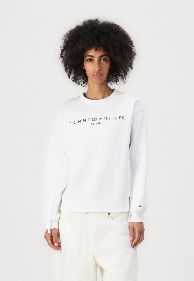 Bijela dukserica od mješavine pamuka s rebrastim rukavima i donjim rubom. Sadrži crni logo "TOMMY HILFIGER EST. 1985" sprijeda.