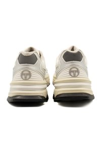 Weiße Sportschuhe mit grauen Akzenten, ausgestattet mit einem strukturierten Obermaterial, gepolsterten Sohlen und einem Logodetail an der Ferse.