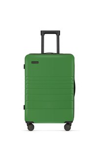 Groene harde koffer met een glad oppervlak, horizontale ribbels, telescopische zwarte handgreep en vier zwarte wielen voor mobiliteit.