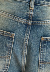 Ljust blå denimjeans med två bakfickor, synlig sömnad och en något använd textur, vilket betonar en avslappnad design.