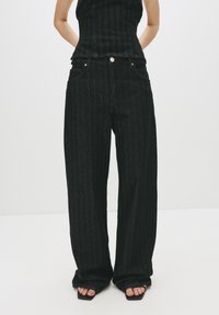 Jeans neri a gamba larga con motivo a righe verticali, realizzati in denim. Presentano un classico design a cinque tasche, chiusura con bottone e vestibilità ampia.