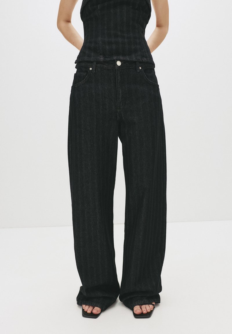 Jeans neri a gamba larga con motivo a righe verticali, realizzati in denim. Presentano un classico design a cinque tasche, chiusura con bottone e vestibilità ampia.