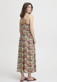 Rochie maxi florală cu spate elastic, bretele subțiri și un model colorat de flori roz, galbene și albe pe un fundal închis.