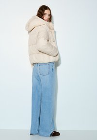 Geacă puf crem cu glugă, cu un model matlasat. Asortată cu blugi largi de culoare albastru deschis și papuci maro pufoși.