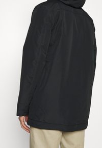 Czarna wodoodporna kurtka z kapturem, o gładkiej fakturze i kieszeniach w szwach bocznych, pokazana od tyłu na jasnym tle.