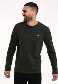 Camicia a maniche lunghe di colore verde oliva realizzata in tessuto morbido, con scollatura a girocollo e una piccola etichetta con logo sul lato sinistro del petto.