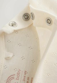 Close-up of white baby garment with small eyelet pattern and metal snap buttons along the fabric edge.