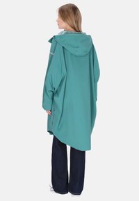 Jachetă de ploaie supradimensionată de culoare albastru-verzui, cu glugă, prevăzută cu fermoar frontal, capse pe laterale și textură netedă, rezistentă la apă.
