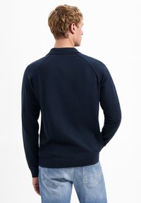 Marineblauwe gebreide pullover met lange mouwen, geribbelde manchetten en kraag. Beschikt over een gladde textuur en een getailleerd ontwerp.