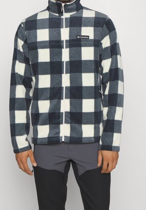 Man draagt een zwart-wit geruit Columbia fleecejack met een volledige ritssluiting aan de voorkant en donkergrijze broek.