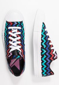 Bunte Leinensneaker mit einem Zickzackmuster in Blau, Rot und Pink, ausgestattet mit weißen Schnürsenkeln und Gummisohlen. Akzentuiert mit schwarz-weißen Details.