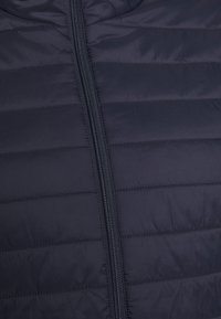 Gepolsterte Jacke in Dunkelblau, mit horizontalen Nähten, Frontreißverschluss und glatter, leicht glänzender Textur. Keine weiteren Details sichtbar.