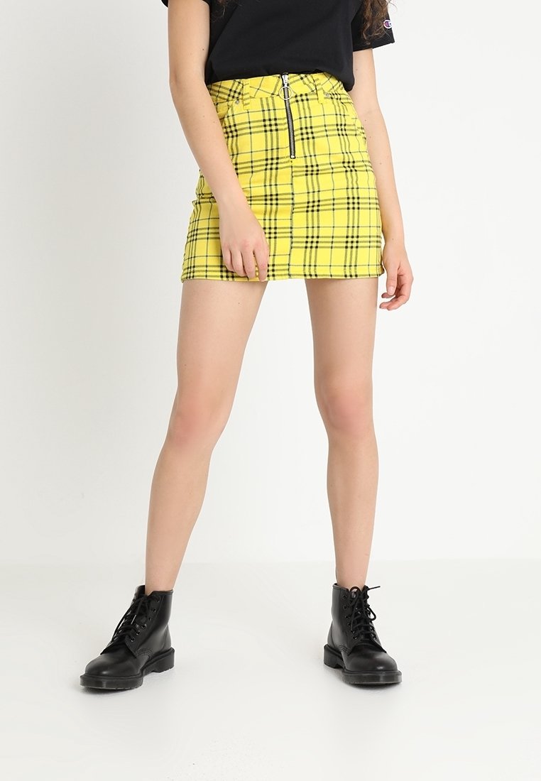 Gul rutigt mini kjol med en frammanskningsdragkedja och ringdragning, parat med svarta snörade ankelstövlar. Slät yta och åtsittande passform.