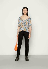 Blusa floral com decote em V, mangas curtas e bainha peplum nas cores azul, laranja e verde, combinada com calças pretas e uma mala laranja.