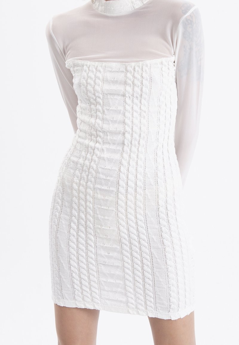 Mini-robe blanche avec un motif tricoté texturé, dotée d'une superposition transparente à manches longues et d'un col montant.