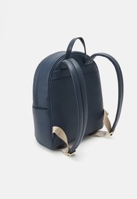 Zaino in pelle blu navy con forma arrotondata, dotato di due maniglie superiori, spallacci regolabili e una finitura testurizzata.
