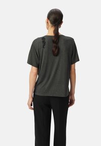 T-shirt gris foncé à manches courtes, texture lisse, coupe décontractée, avec des accents décoratifs dans la partie supérieure du dos ; associé à un pantalon noir.