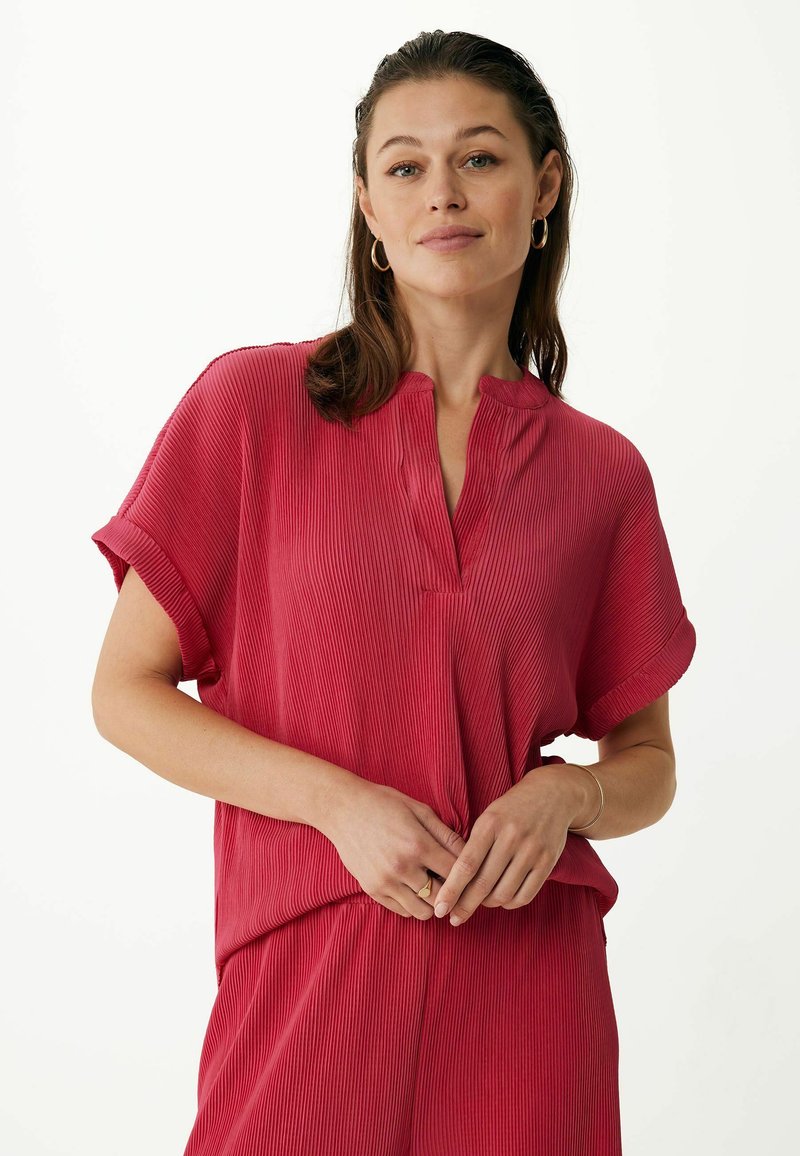 Červený žebrovaný top s krátkým rukávem a mandarínským límcem. Má uvolněný střih a jemnou texturu. Kombinováno s odpovídajícími kalhotami.