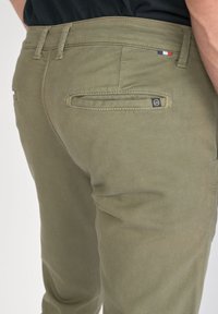 Pantalons en mélange de coton vert olive avec une texture lisse ; dotés de deux poches arrière et d'un petit logo de marque près de la taille.