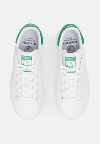 Pár bílých tenisek Adidas Stan Smith se zelenými patními tabulkami, bílými tkaničkami a zelenými logy na jazyku, pohled shora.
