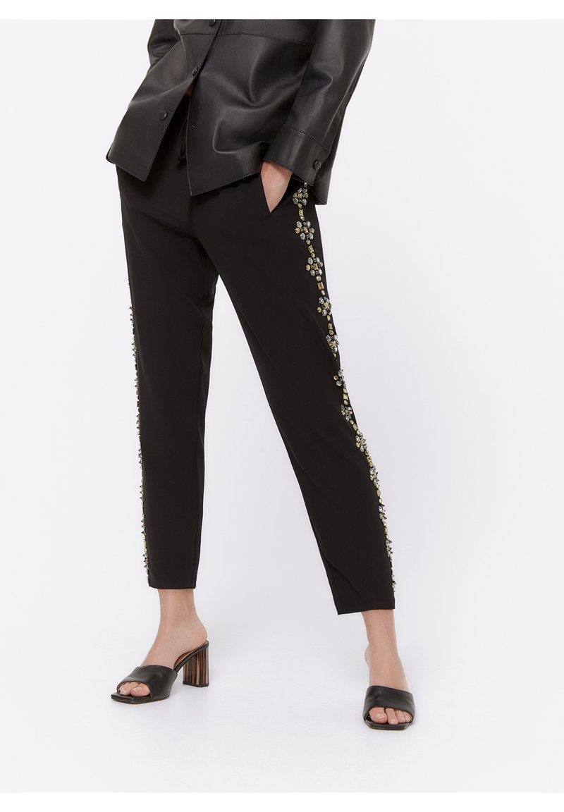 Zwarte broek met versierde side-details, waaronder kralen en bloemmotieven. Slim-fit ontwerp met een gladde stoftextuur.