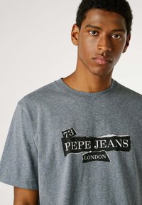 Sivé bavlnené tričko s čiernou grafickou potlačou s textom „73 PEPE JEANS LONDON“. Krátke rukávy a okrúhly výstrih.
